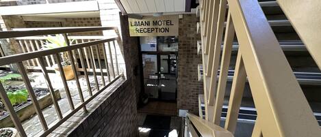 Una zona de recepción con un letrero del motel Limani, una escalera y vistas del área exterior con plantas en macetas.