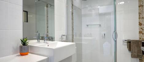 Un baño moderno con cabina de ducha de vidrio, un lavabo blanco con una planta y un espejo.