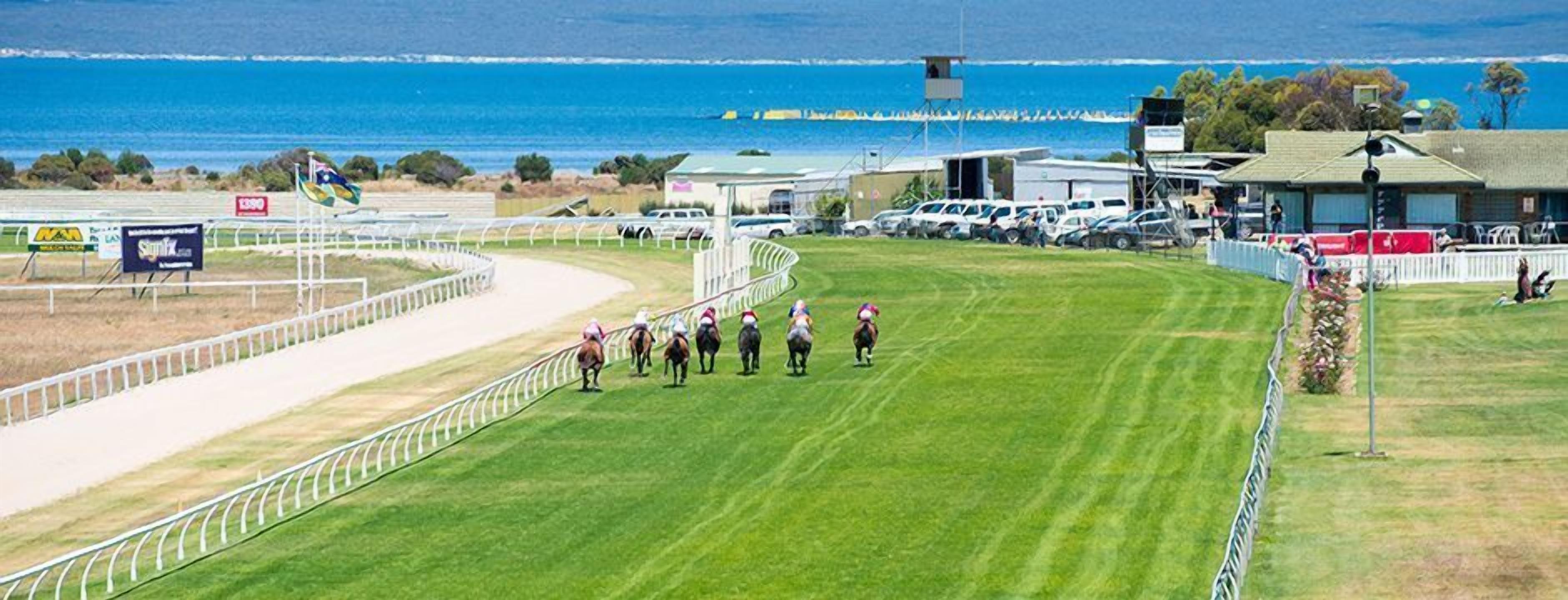 A horse race track with a coastal view, a fenced area, and a few parked cars.