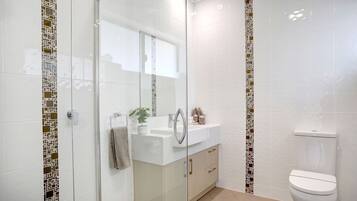 A modern bathroom with a glass shower enclosure, a white sink with a mirror, and a toilet.