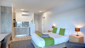 A modern hotel room with a bed, bedside tables, a desk, and a kitchenette.