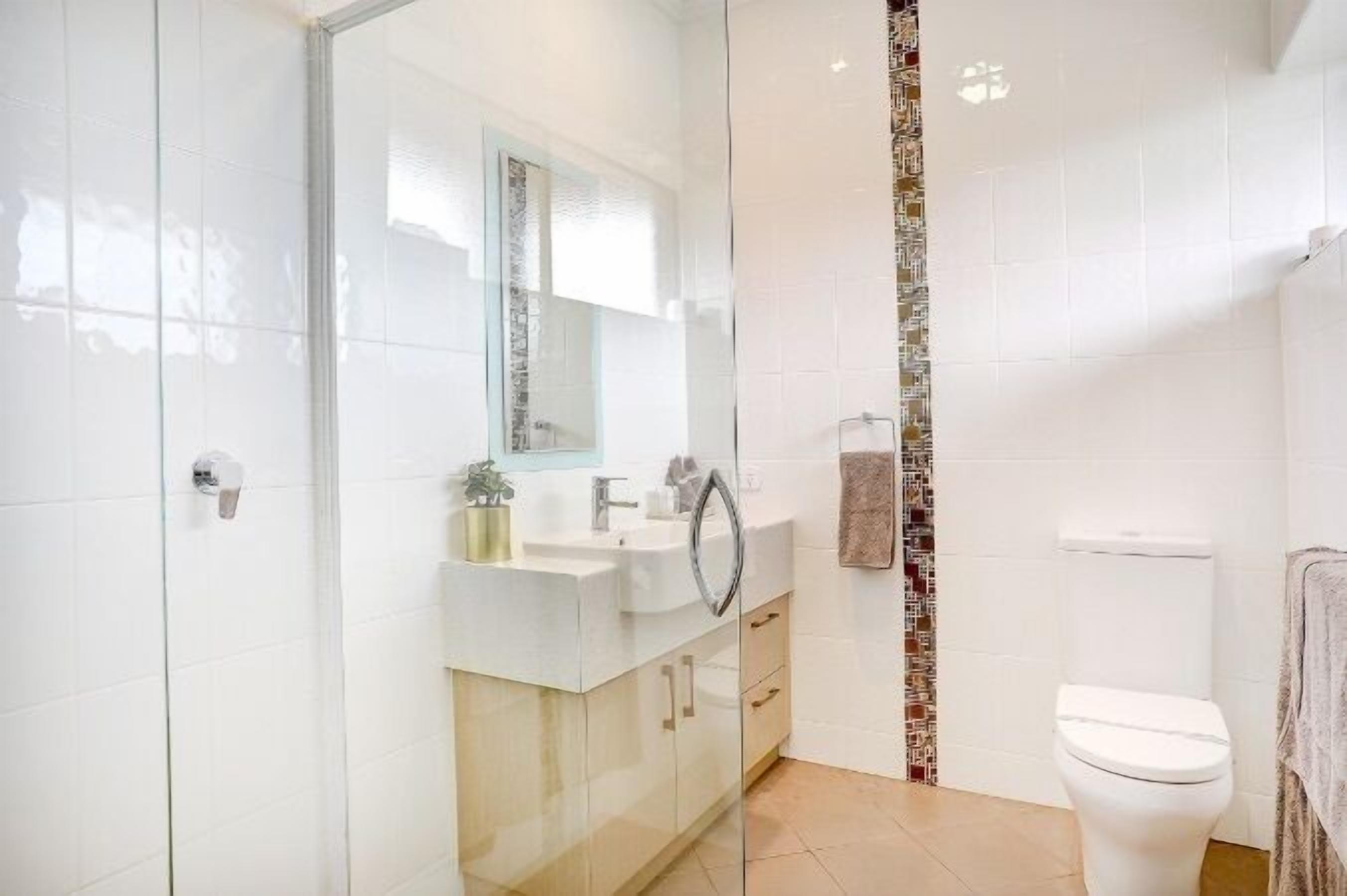 A modern bathroom with a glass shower enclosure, a white sink with a mirror, and a toilet.