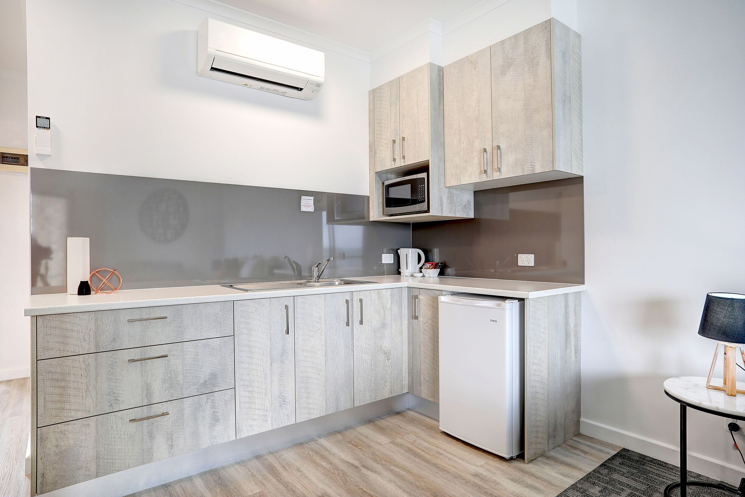Una cucina moderna con mobili grigi, un forno a microonde integrato e un piccolo frigorifero.