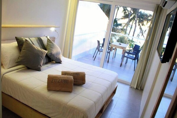 A hotel room with a bed, pillows, and a view of the outdoor area through a sliding glass door.