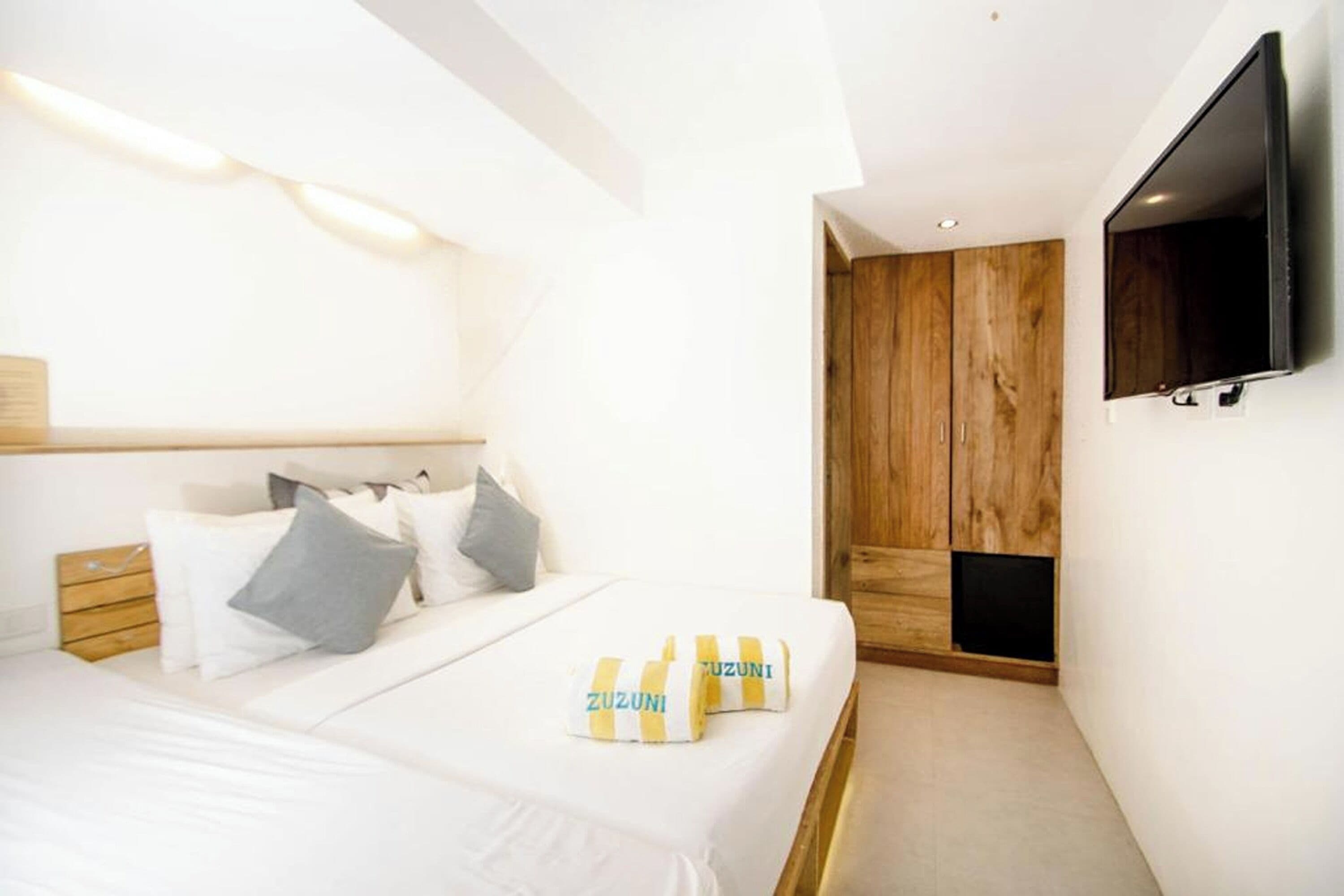 Un dormitorio moderno con cama, almohadas, televisión y armario.