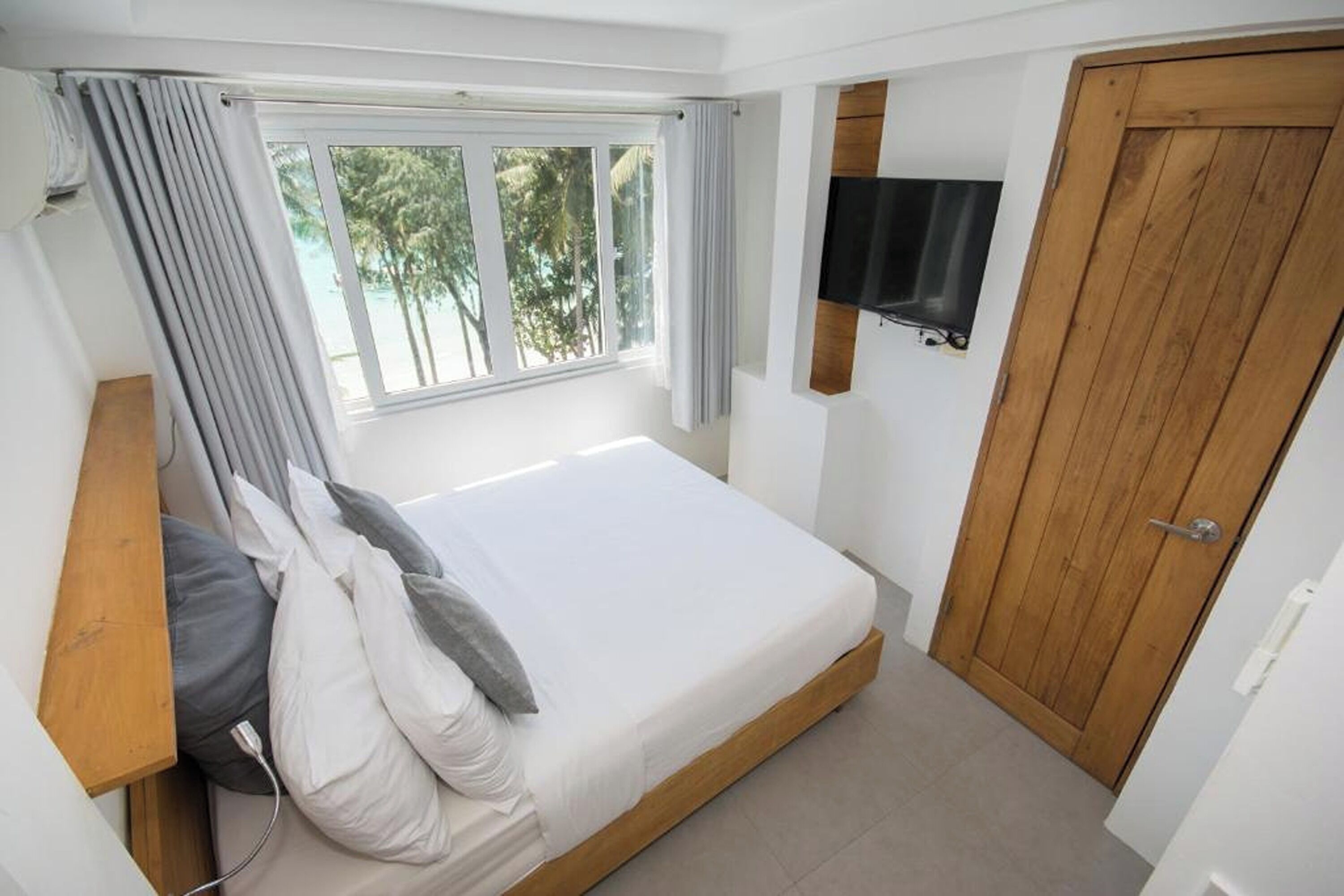 A bedroom with a single bed, a wooden headboard, a TV mounted on the wall, and a wooden door.
