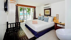A hotel room with a large bed, a bench, a TV, a wooden nightstand, and a view of the beach. - Zuzuni Boutique Hotel (Boracay Island)