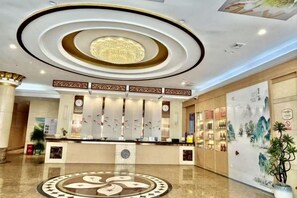 A hotel lobby with a reception desk, a circular decorative floor pattern, and a large poster on the wall.