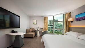 Habitació d'hotel amb llit, televisió, sofà, taula petita i finestra amb vista a la ciutat.