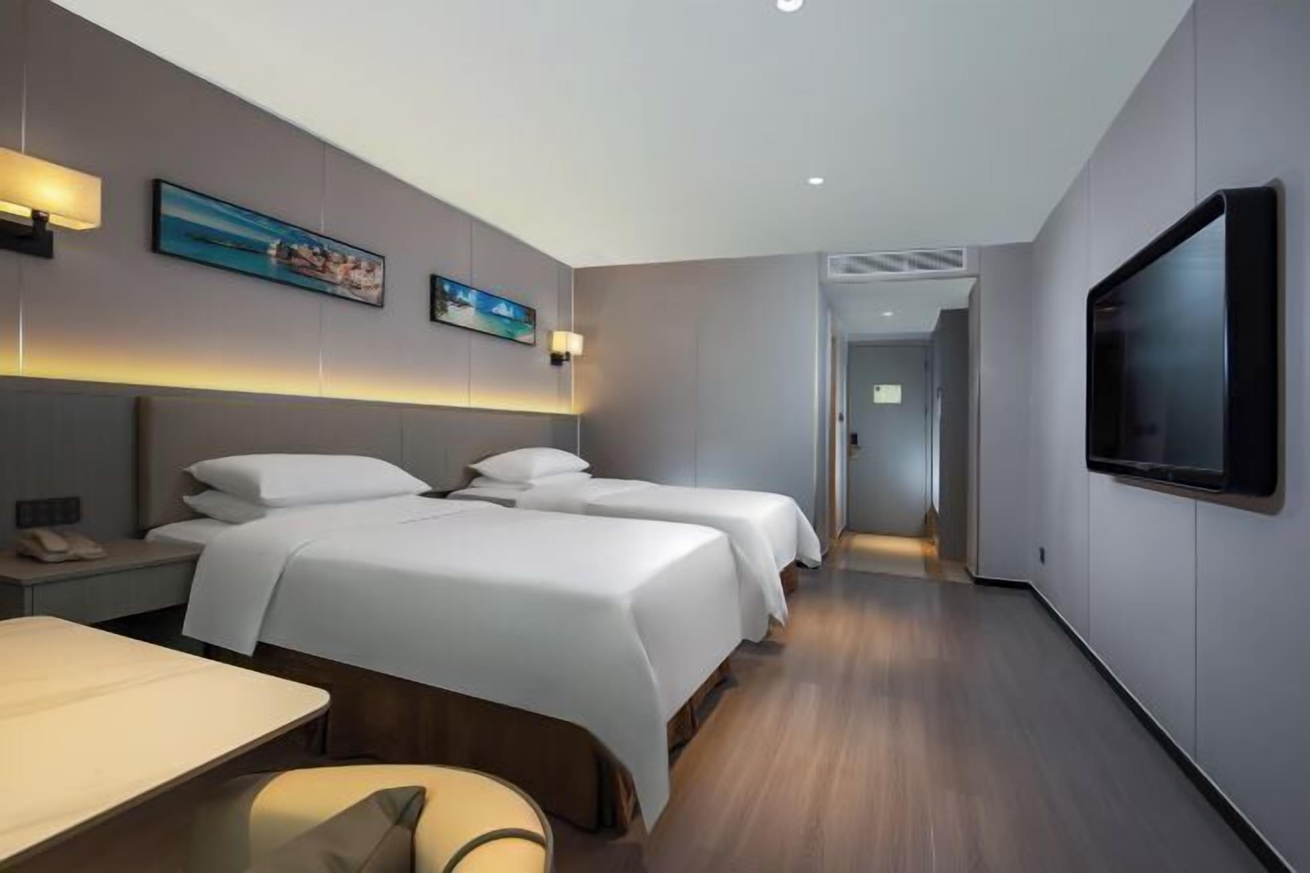 A hotel room with two beds, a desk, a chair, a TV, and artwork on the walls.