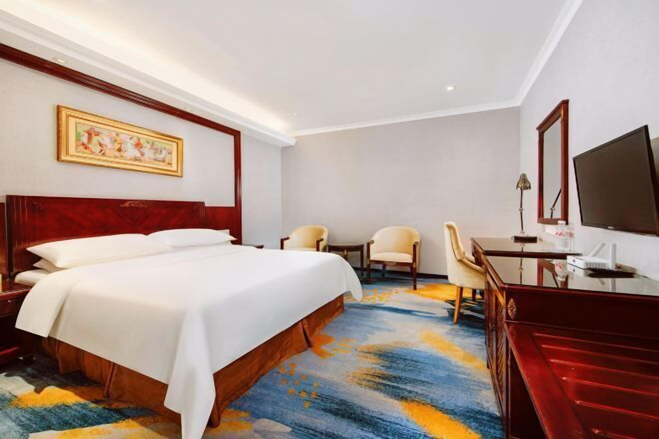 A hotel room with a large bed, two chairs, a desk, and a television.