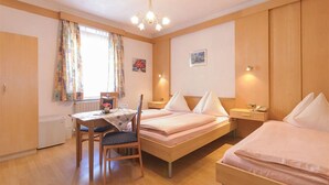 A hotel room with two single beds, a wooden table with a chair, a small desk, and a window with curtains. - Tautermann Garni (Innsbruck)