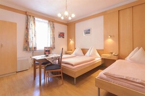Una habitación de hotel con dos camas individuales, una mesa de madera con una silla, un escritorio pequeño y una ventana con cortinas.