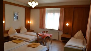 A hotel room with two single beds, a small table with chairs, a window with curtains, and wall-mounted lights. - Tautermann Garni (Innsbruck)