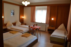 Habitación de hotel con dos camas individuales, una mesa pequeña con sillas, una ventana con cortinas e iluminación en la pared.