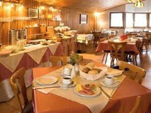 Un comedor con varias mesas dispuestas para el desayuno, con pan, bollería y café.