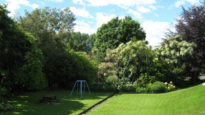 A grassy area with a swing set, a picnic table, and a small wooden bridge over a drainage ditch. - Golden Bay Motel (Takaka)