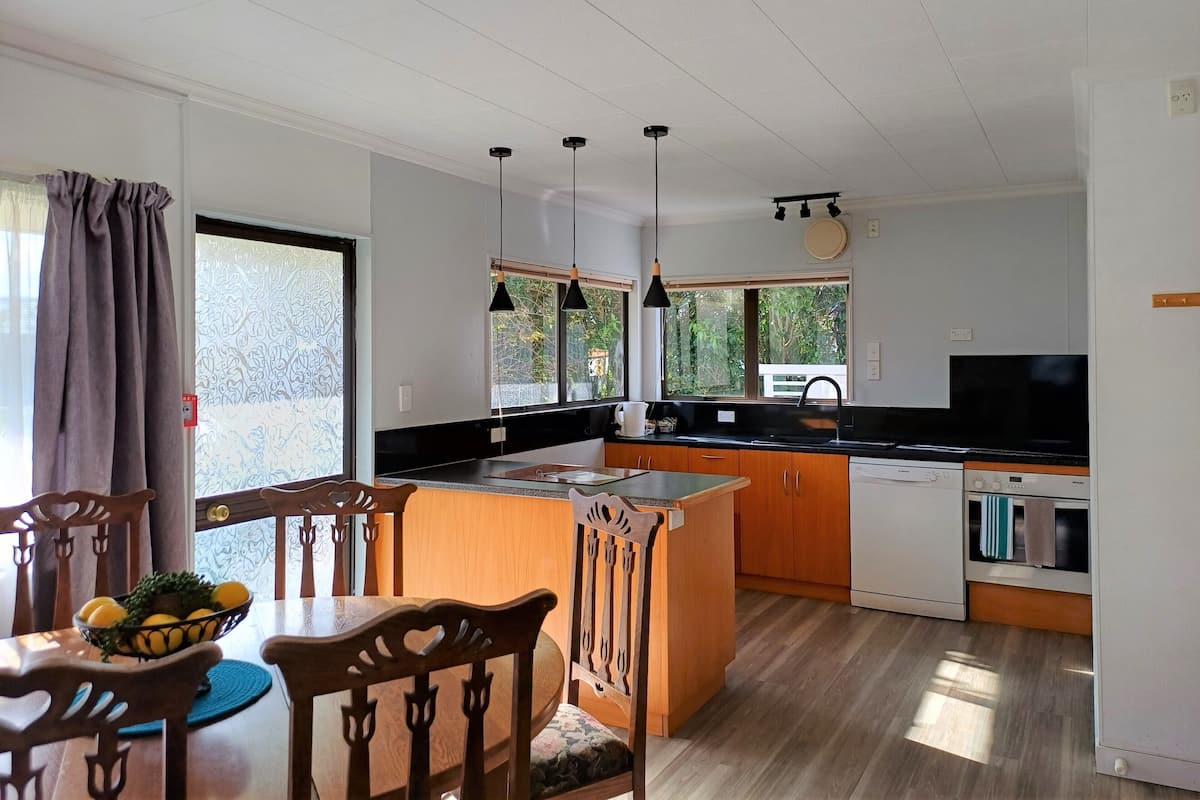 A modern kitchen with wooden cabinets, a black countertop, and pendant lighting.