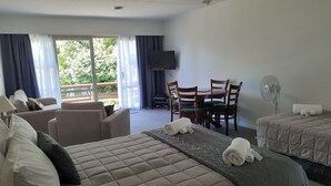 A hotel room with a bed, a sofa, a dining table with chairs, a TV, and a fan. - Golden Bay Motel (Takaka)