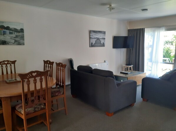 A living room with a sofa, a dining table with chairs, a flat-screen TV, and artwork on the walls.