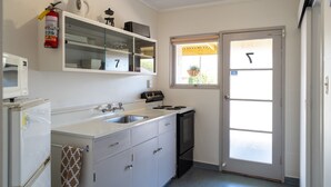 A compact kitchen with a refrigerator, stove, sink, and a window with a view of the outside. - Golden Bay Motel (Takaka)