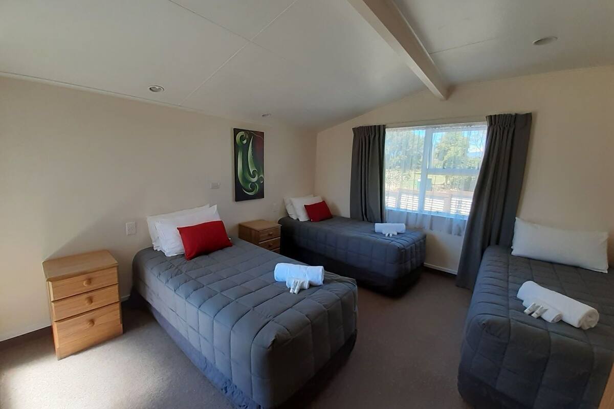 A hotel room with three beds, a wooden nightstand, and a window with curtains.