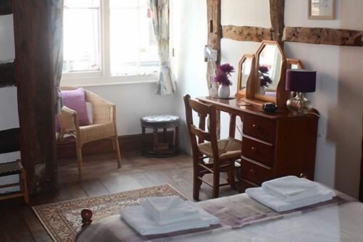 A bedroom with a bed, wooden dresser, chair, and a small table with a lamp.