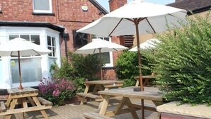 Un espace extérieur aménagé en terrasse, avec des tables de pique-nique en bois et des parasols blancs.
