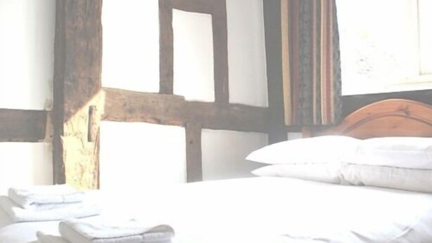 Une chambre avec une tête de lit en bois, un lit bien fait avec du linge de maison blanc, et une fenêtre avec des rideaux.
