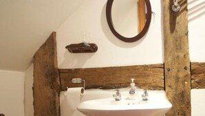 Une salle de bain avec un lavabo blanc, des poutres en bois, un miroir et un distributeur de serviettes.
