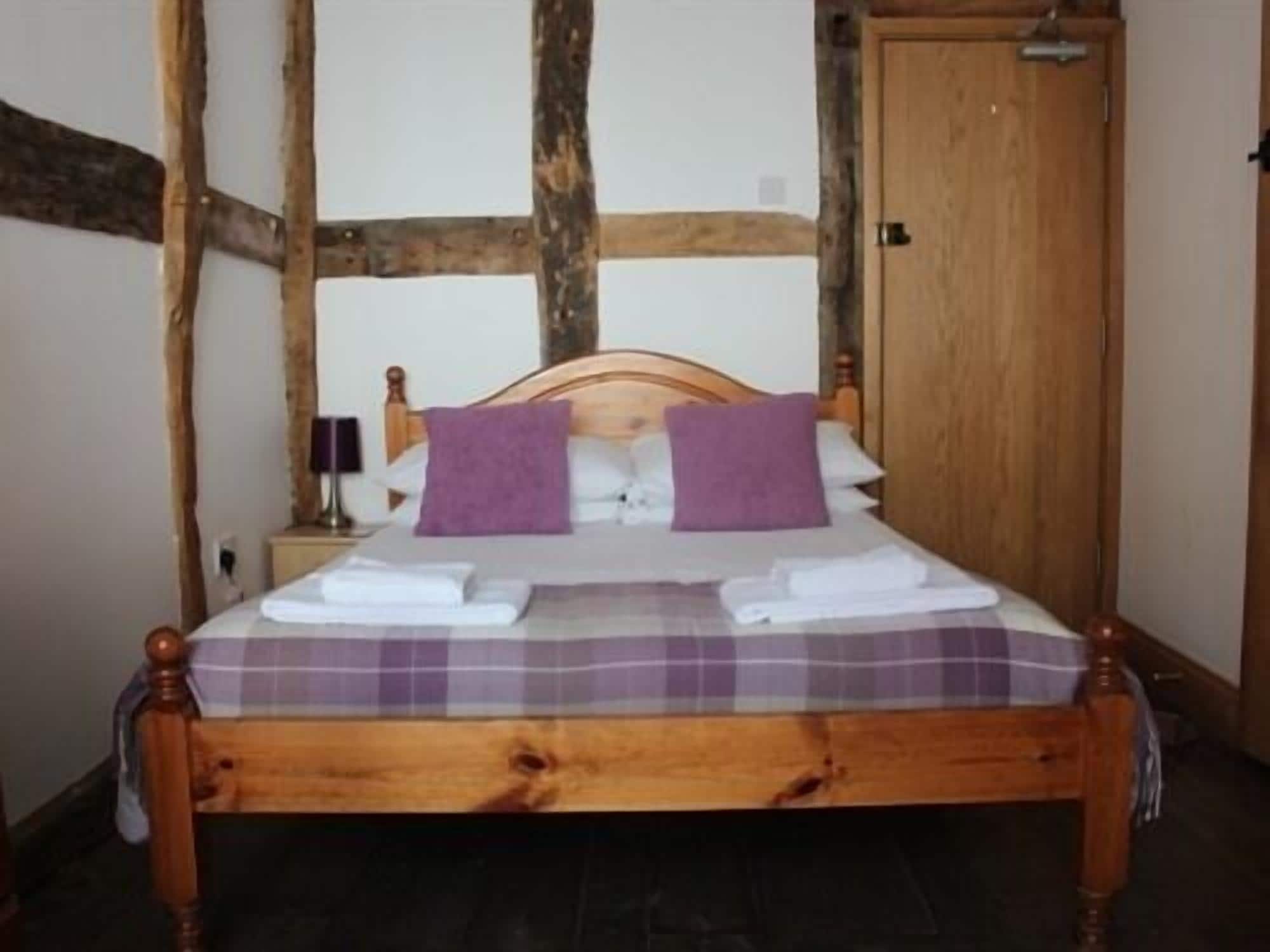 Un lit à baldaquin en bois, recouvert d’une courtepointe à carreaux et agrémenté de deux coussins violets.