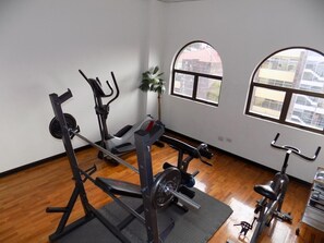 Ein Fitnessraum mit Trainingsgeräten, einer Bank und großen Fenstern.