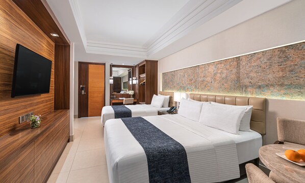 A modern hotel room with two beds, a flat-screen TV, a large abstract painting, and a dining area with a fruit plate. - Henann Prime Beach Resort (Boracay Island)