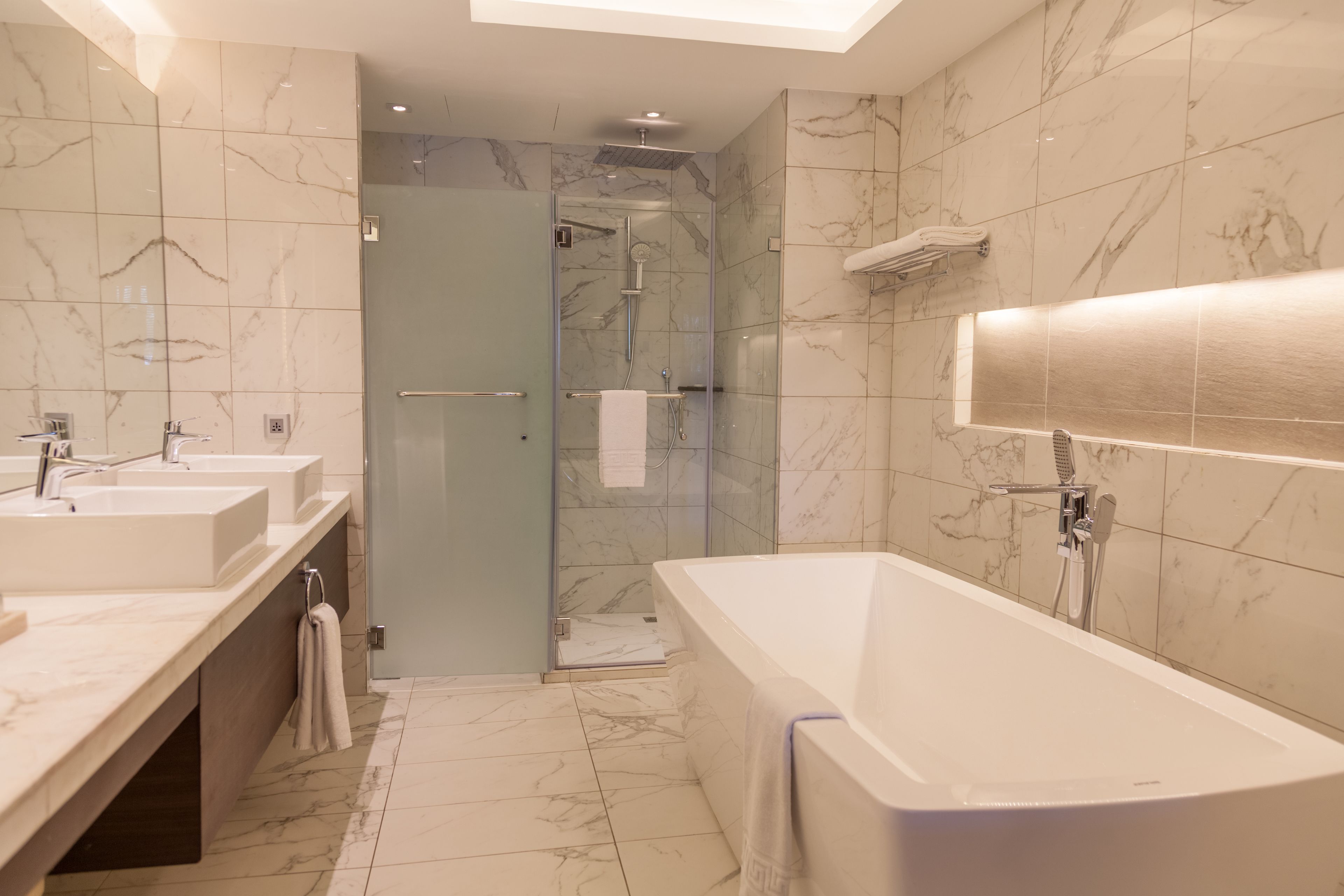 Un bagno moderno con una vasca da bagno ampia, due lavabi, cabina doccia in vetro e pavimento in marmo.
