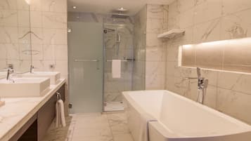 Un baño moderno con una bañera grande, dos lavamanos, mampara de vidrio para la ducha y suelo de mármol.