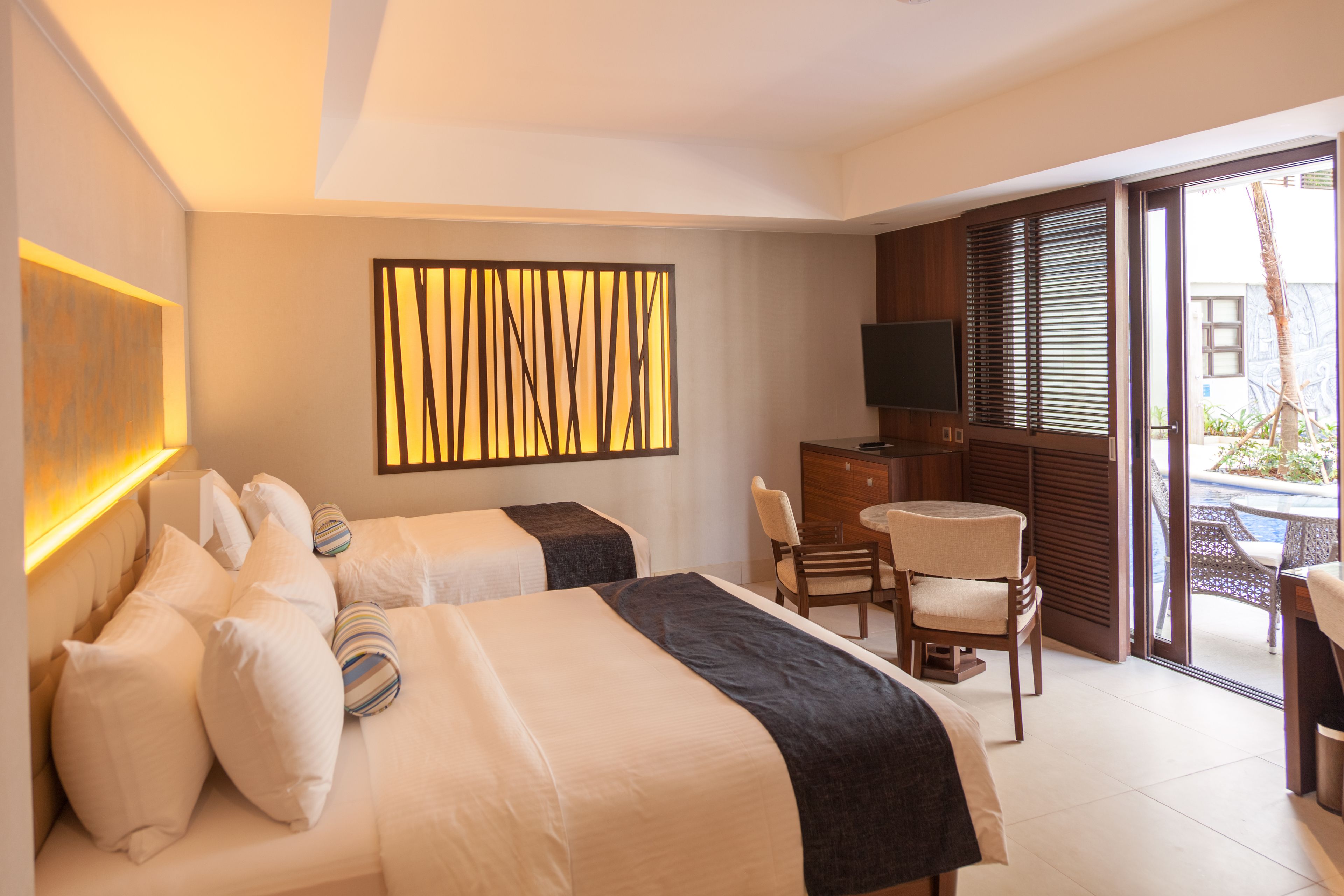 Habitación de hotel con dos camas, televisión, escritorio y vista al exterior.