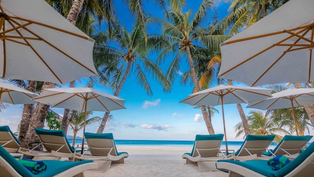 A beach with white lounge chairs and umbrellas, palm trees, and a clear blue sky. - Henann Prime Beach Resort (Boracay Island)