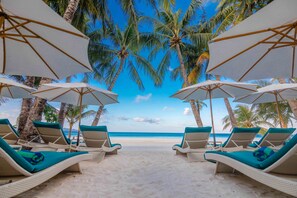 A beach with white lounge chairs and umbrellas, palm trees, and a clear blue sky. - Henann Prime Beach Resort (Boracay Island)