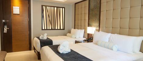 A hotel room with two beds, a wooden door, a wall-mounted air conditioner, a decorative panel, and a bedside lamp.