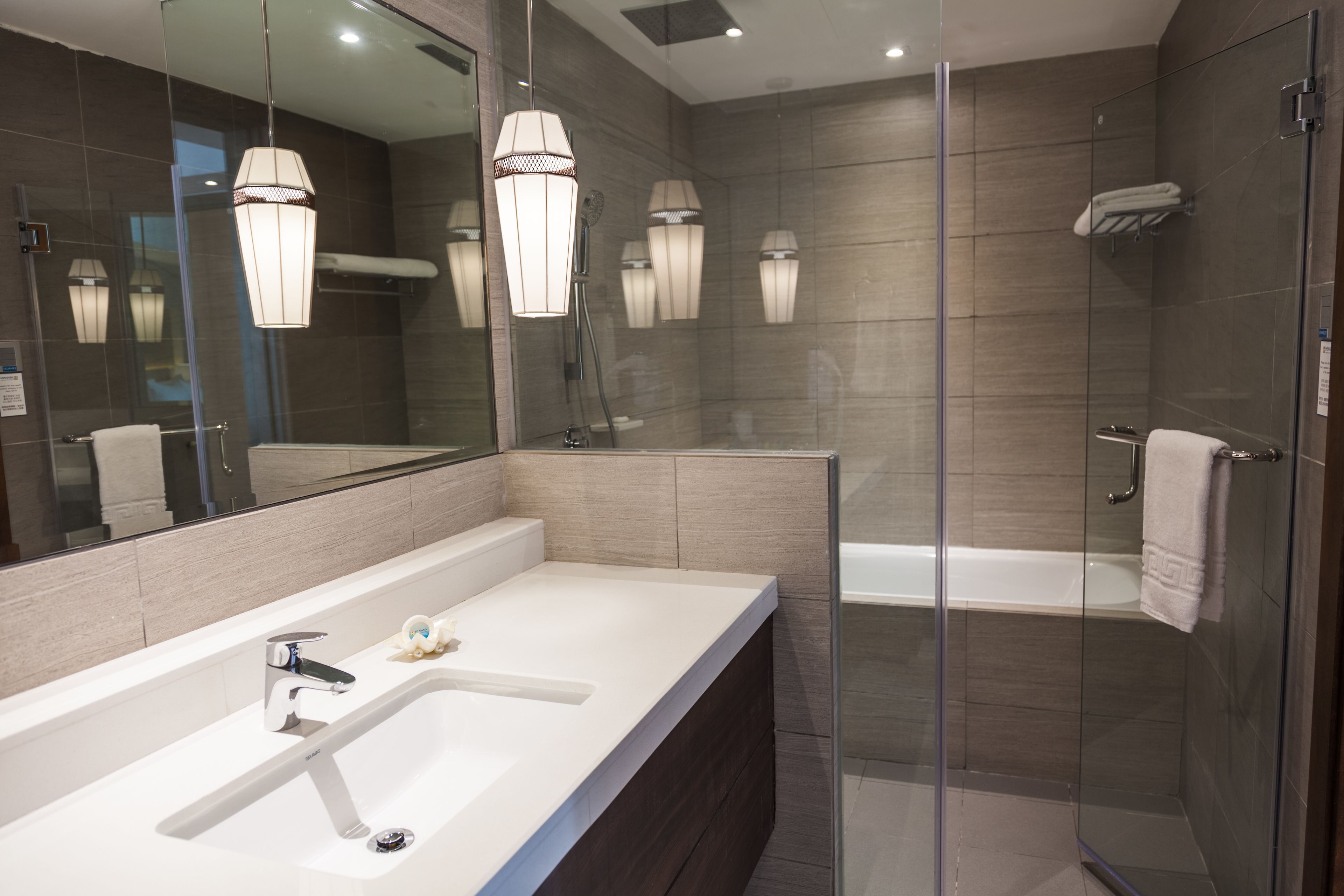 A modern bathroom with a large mirror, a white sink, a shower enclosure, and a bathtub.