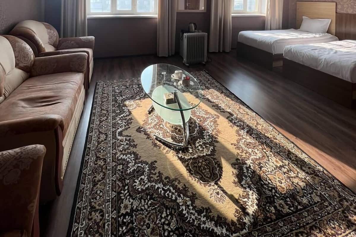 Hotellihuone, jossa on sohva, kaksi sänkyä, lasinen sohvapöytä ja kuviollinen matto.