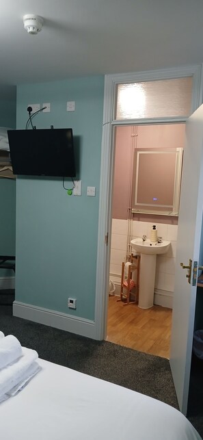 A room with a bed, a mounted TV, a door leading to a bathroom with a sink and mirror. - The Crafty Cow (Bristol)