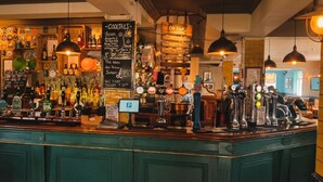 A bar area with a counter, various bottles, a chalkboard menu, and a private section. - The Crafty Cow (Bristol)