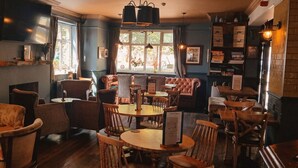 A cozy restaurant interior with wooden tables and chairs, framed pictures on the walls, and a window providing natural light. - The Crafty Cow (Bristol)