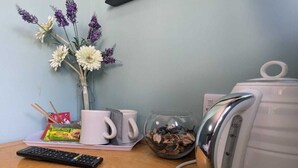 Un bureau avec une télécommande, un vase rempli de fleurs, une bouilloire et une tasse.