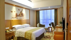 A hotel room with a large bed, a desk with a telephone, a chair, a television, and a window with curtains. - Vienna International Hotel (Changsha)