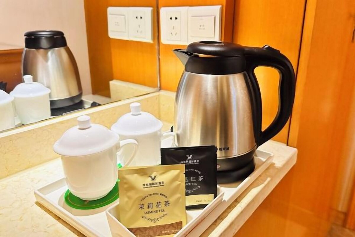 A tea station with a stainless steel kettle, a white teapot, a white teacup, a green tea infuser, and two tea bags labeled 'Jasmine Tea'.