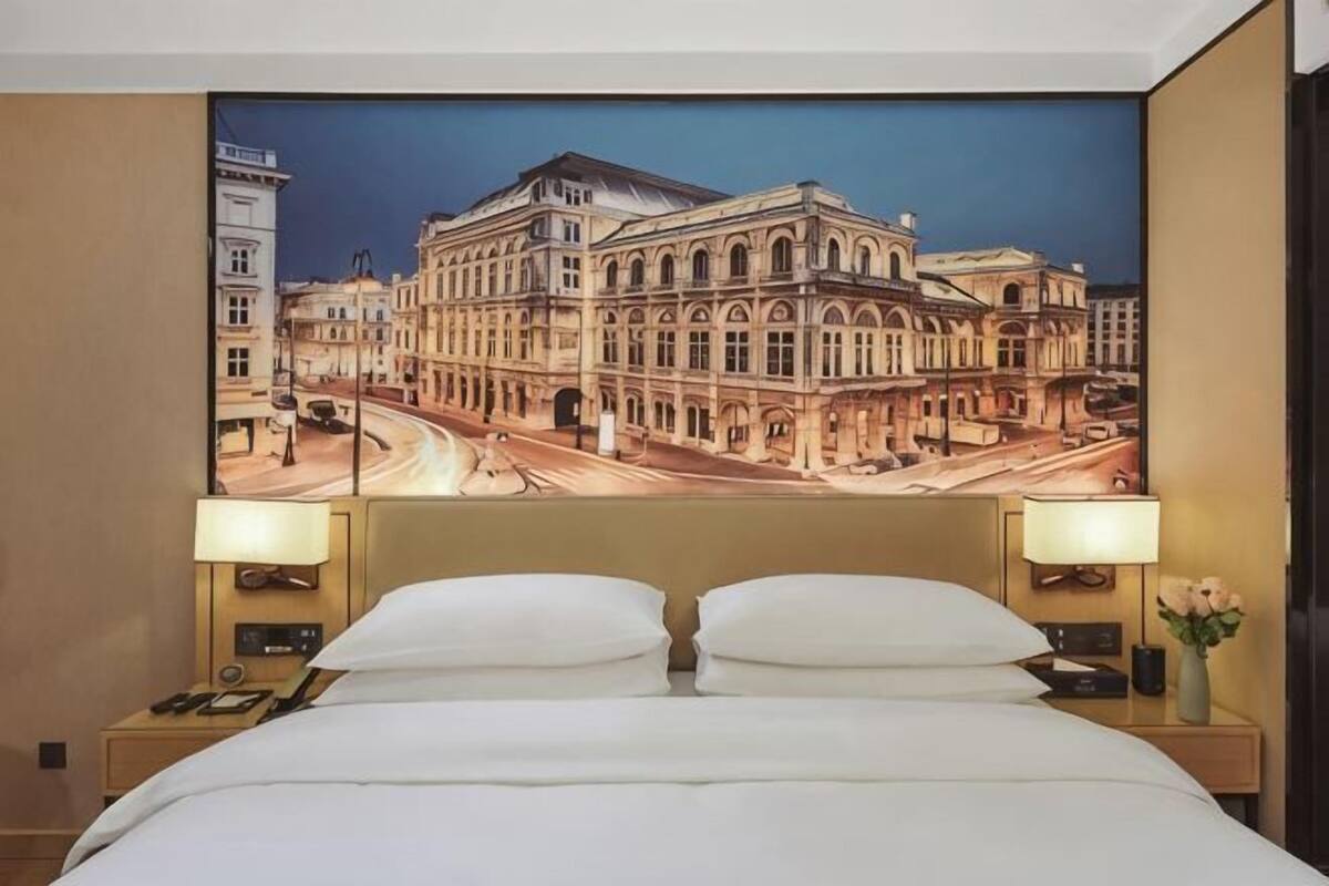 A hotel room with a large bed, two bedside tables with lamps, and a large wall mural of a building.