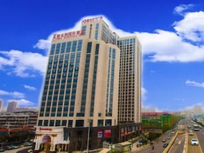 A multi-story hotel with a prominent sign at the top, surrounded by a busy urban street with vehicles and other buildings. - Vienna International Hotel (Changsha)