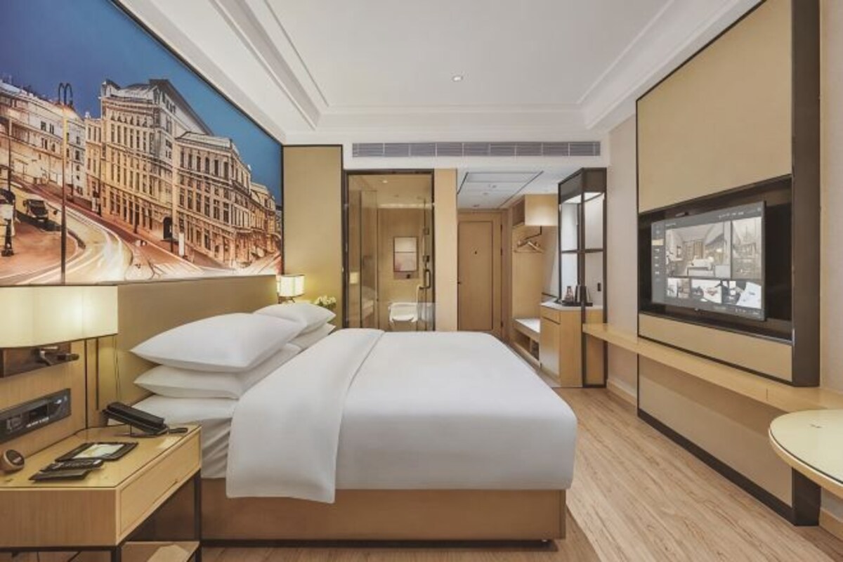 Habitació d'hotel amb un llit, una taula de nit, una làmpada i un finestral gran.